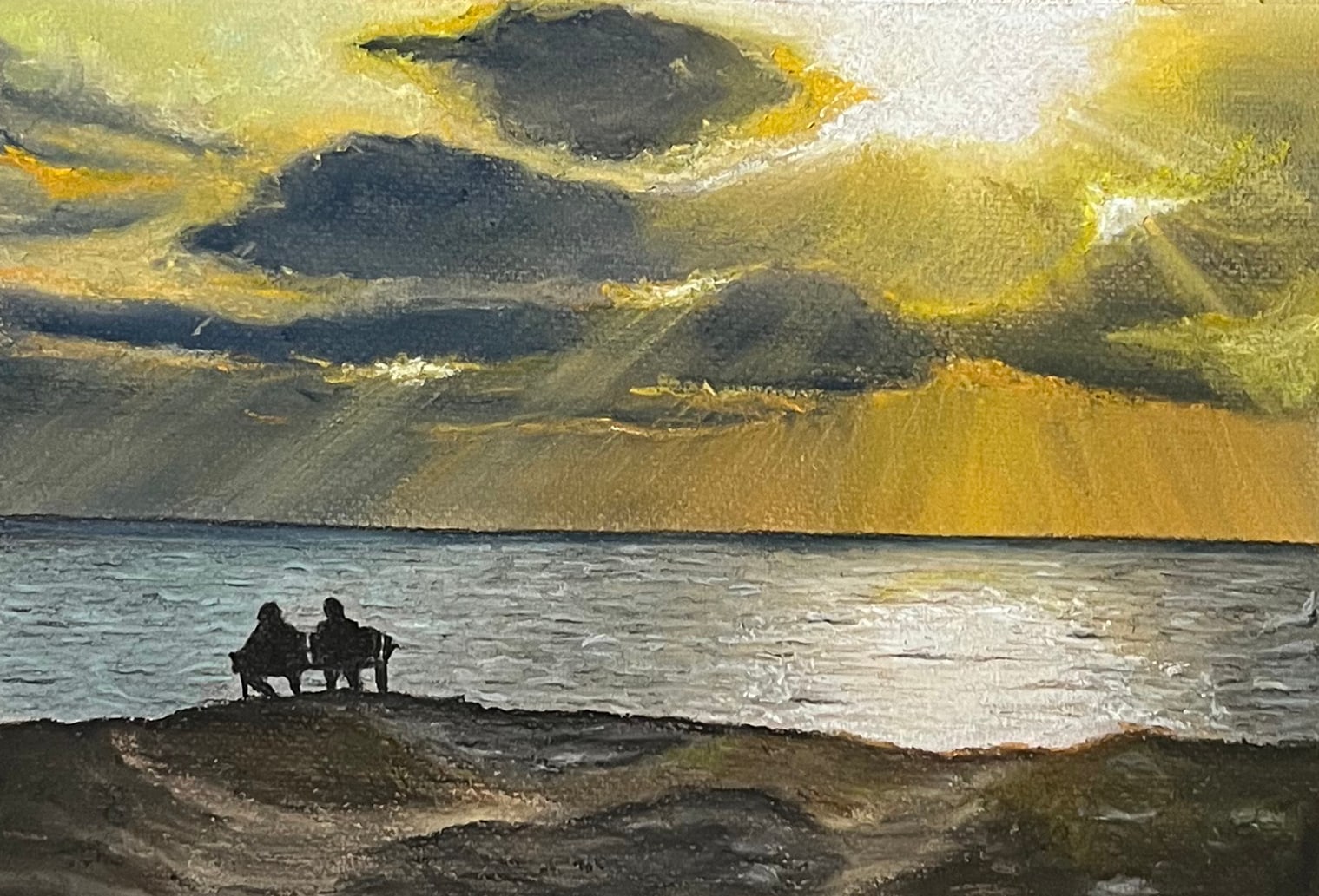 Two people sit together on a bench on a grassy rise, looking out at a silver sea under dark clouds split by shafts of golden light.