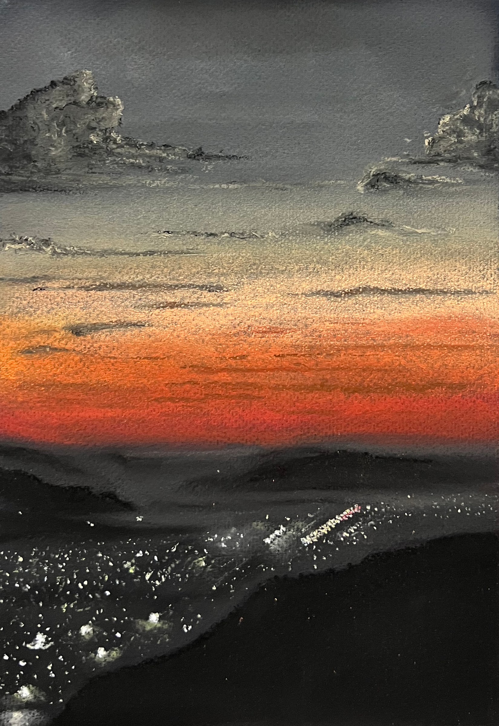 Seen from a hillside at dusk, the lights of a valley city sparkle below a red horizon and slate-grey clouds.